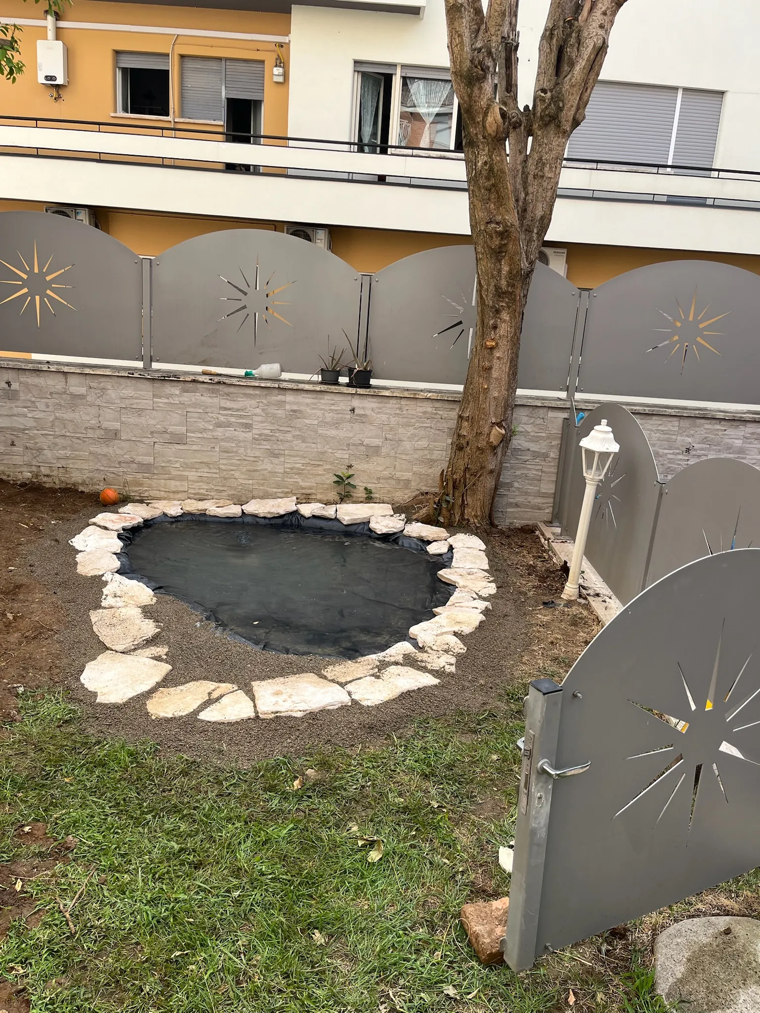 Laghetto ornamentale appena realizzato in un giardino condominiale, con bordo in pietra bianca